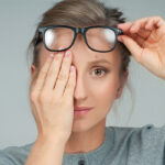 Woman with hand over eye next to an eye chart.